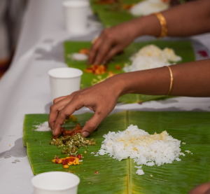 Hände essen traditionelles südindisches Gericht von Bananenblättern, serviert mit Reis und Gemüse in leuchtenden Farben.