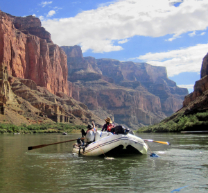 Ein Schlauchboot mit Abenteurern fährt auf dem Colorado River zwischen den steilen, roten Felswänden des Grand Canyon.