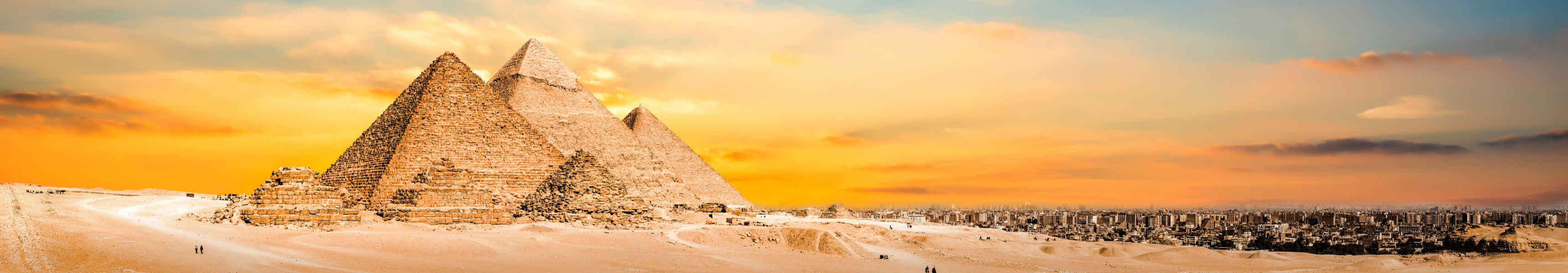 Die Pyramiden von Gizeh in Ägypten bei Sonnenuntergang mit goldfarbenem Himmel und Kamelen in der Wüste