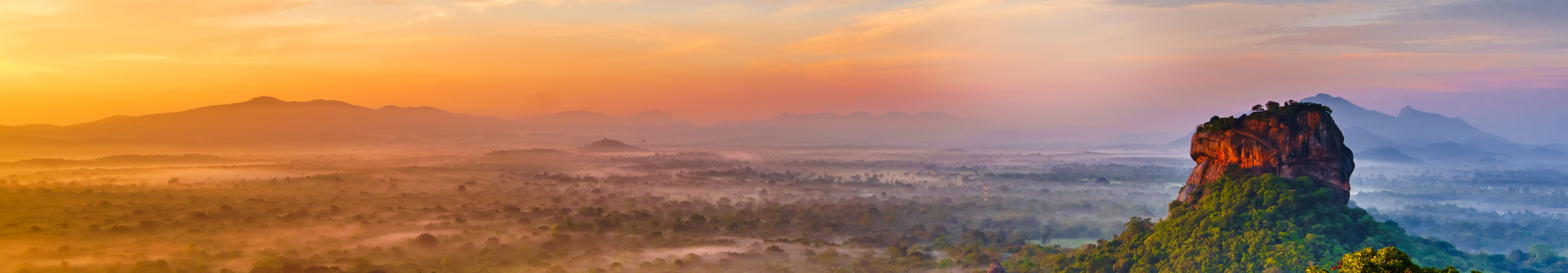 Luftaufnahme des Sigiriya-Felsens in Sri Lanka bei Sonnenaufgang mit gr&uuml;nem Dschungel im Vordergrund und farbenpr&auml;chtigem Himmel im Hintergrund