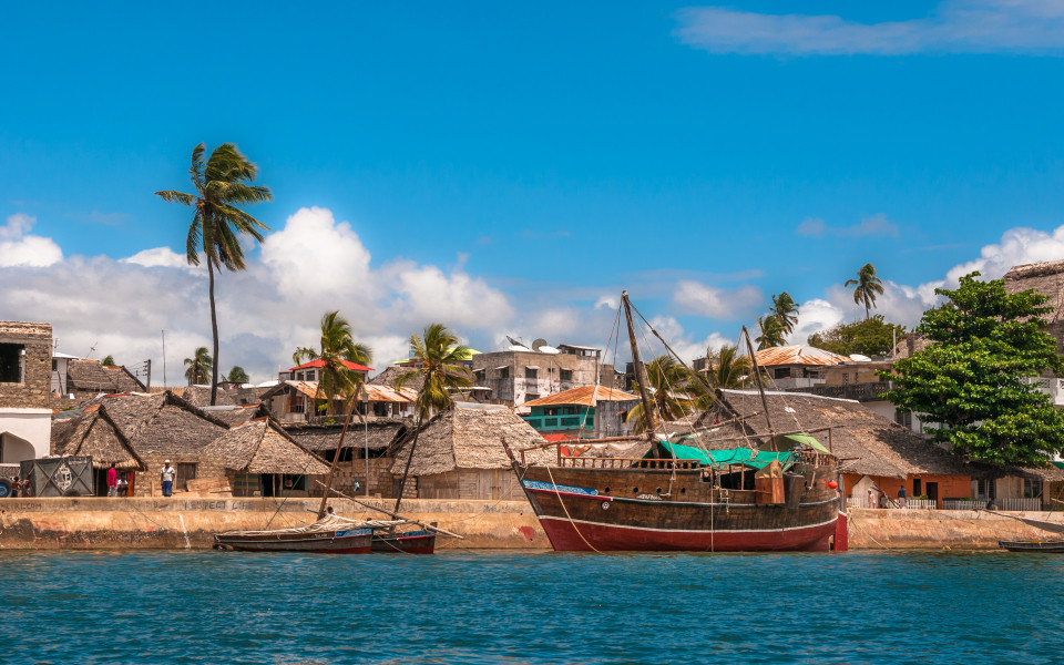 Küste von Lamu mit traditionellen Häusern und einem Holzboot im Vordergrund.